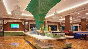 A spacious lobby with a central reception desk, a large screen, and a chandelier.