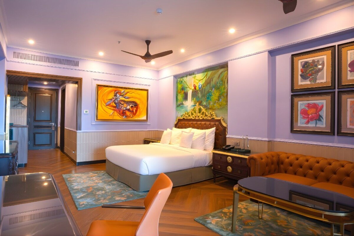 A hotel room with a bed, a sofa, a desk, and artwork on the walls.