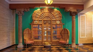 A lobby with a checkered floor, a green wall with a decorative wooden arch, and two ornate chairs.