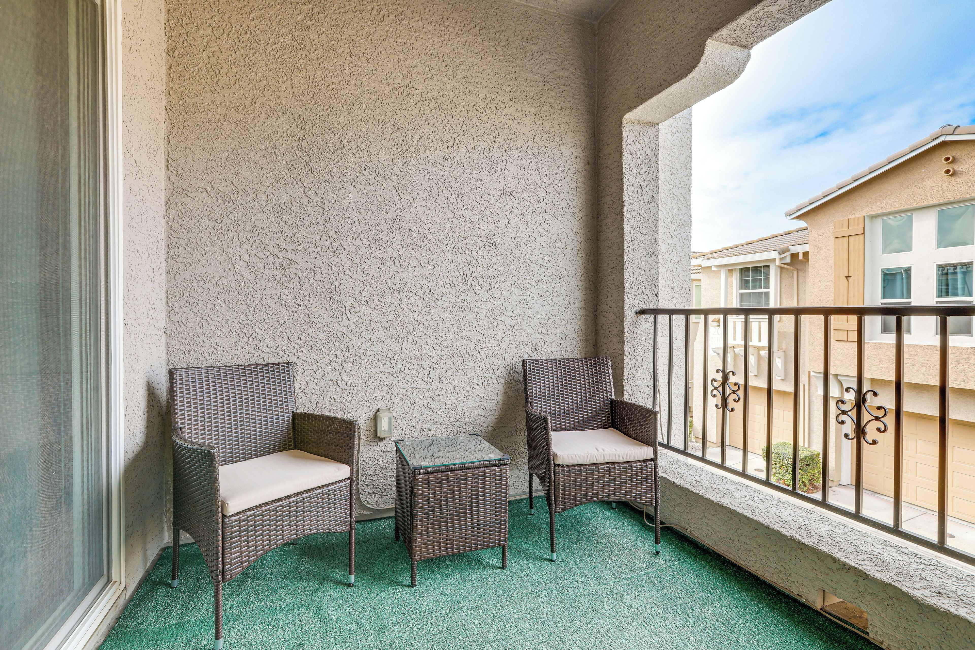 A balcony with two wicker chairs and a small table, a textured wall, and a view of neighboring buildings.
