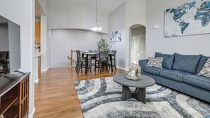Un salon spacieux avec un canapé bleu, une table basse ronde et un coin repas comprenant une table et des chaises en bois.