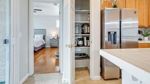 Une cuisine moderne équipée d’appareils électroménagers en acier inoxydable, un garde-manger avec des récipients de rangement, et une chambre à coucher visible à travers une porte ouverte.