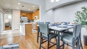 Une cuisine moderne avec des meubles en bois, un îlot central et un coin repas comprenant une table blanche et des chaises grises.
