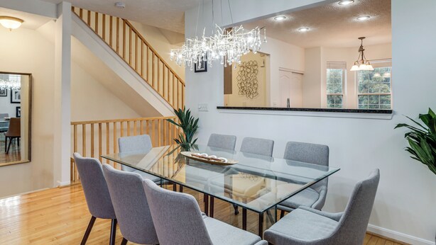 A modern dining area with a glass table and grey chairs, a wooden staircase, and a chandelier. - 1 Mi to Dtwn Cincinnati: Spacious Townhome w/ Deck (Cincinnati)