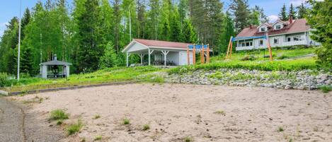 A sandy beach area with a pavilion, a small gazebo, and a house with a red roof.