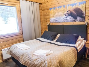A bed with a quilted bedspread and pillows, a window with blinds, and a painting of a bear on the wall. - Vuokatti villas karhu by Interhome (Sotkamo)