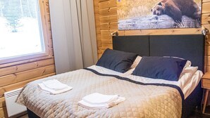 Ein Schlafzimmer einer Holzhütte mit einem Bett, Kissen und einem Bärenbild an der Wand.