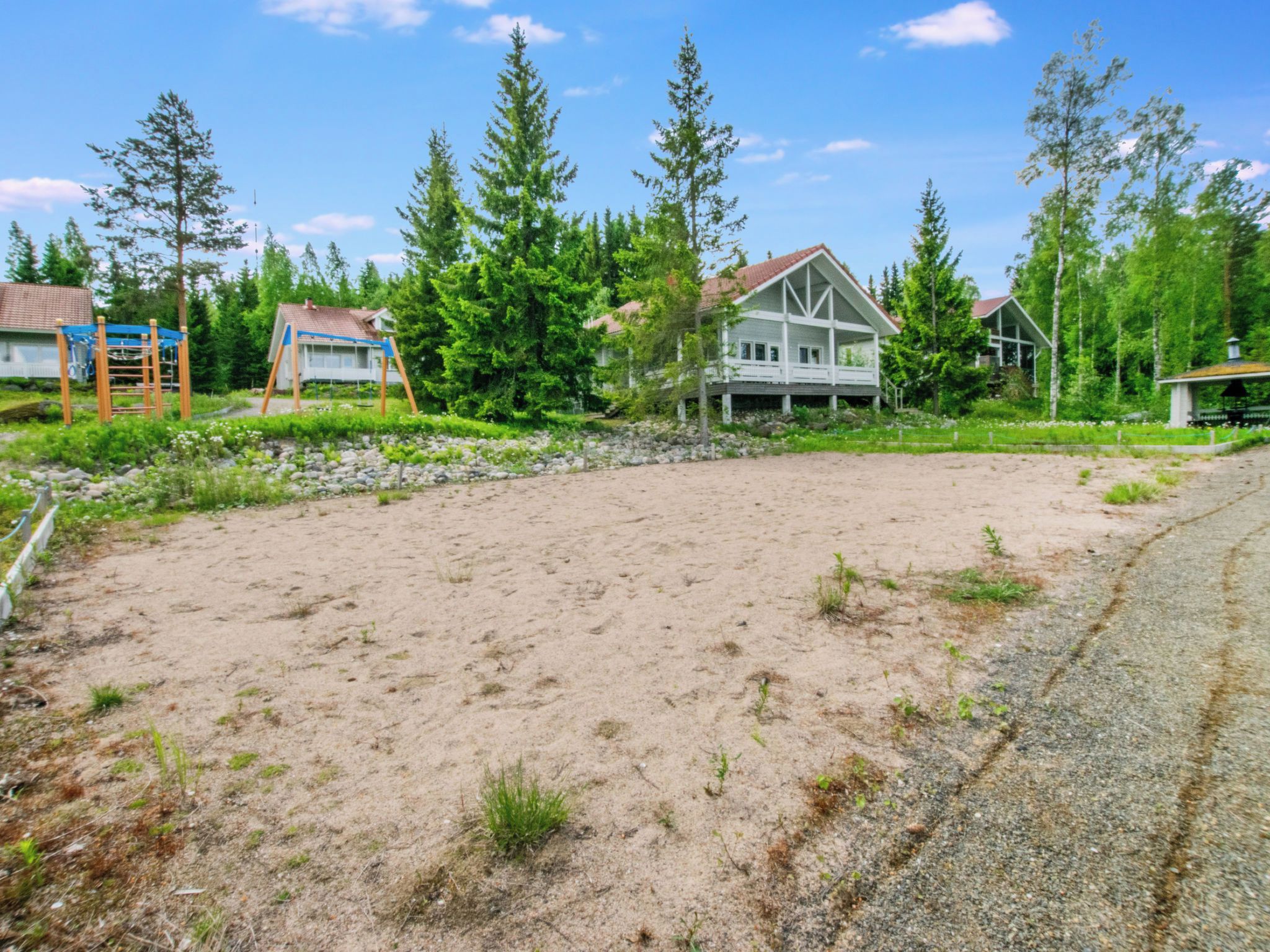 A residential area with a sandy yard, wooden play structures, and houses with red roofs.