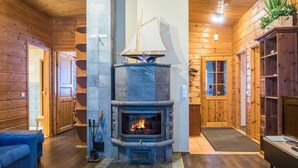 Ein rustikaler Blockhaus-Innenraum mit Kamin aus Naturstein, Holzwänden und einem blauen Sofa.