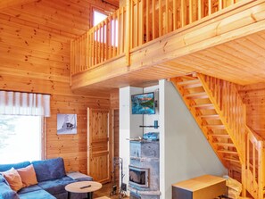 Ein Interieur einer Holzhütte mit einer Couch, einem Kamin und einer Treppe.