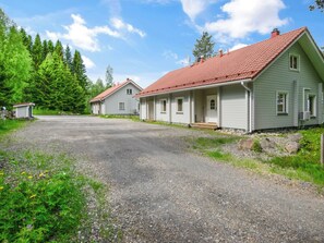 Une maison à deux étages, avec un toit recouvert de tuiles rouges, un porche et une allée gravillonnée.
