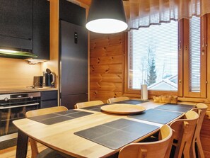 Eine kompakte Küche mit modernen Geräten, ein Essbereich mit Holzzmöbeln und ein großes Fenster mit Jalousien.
