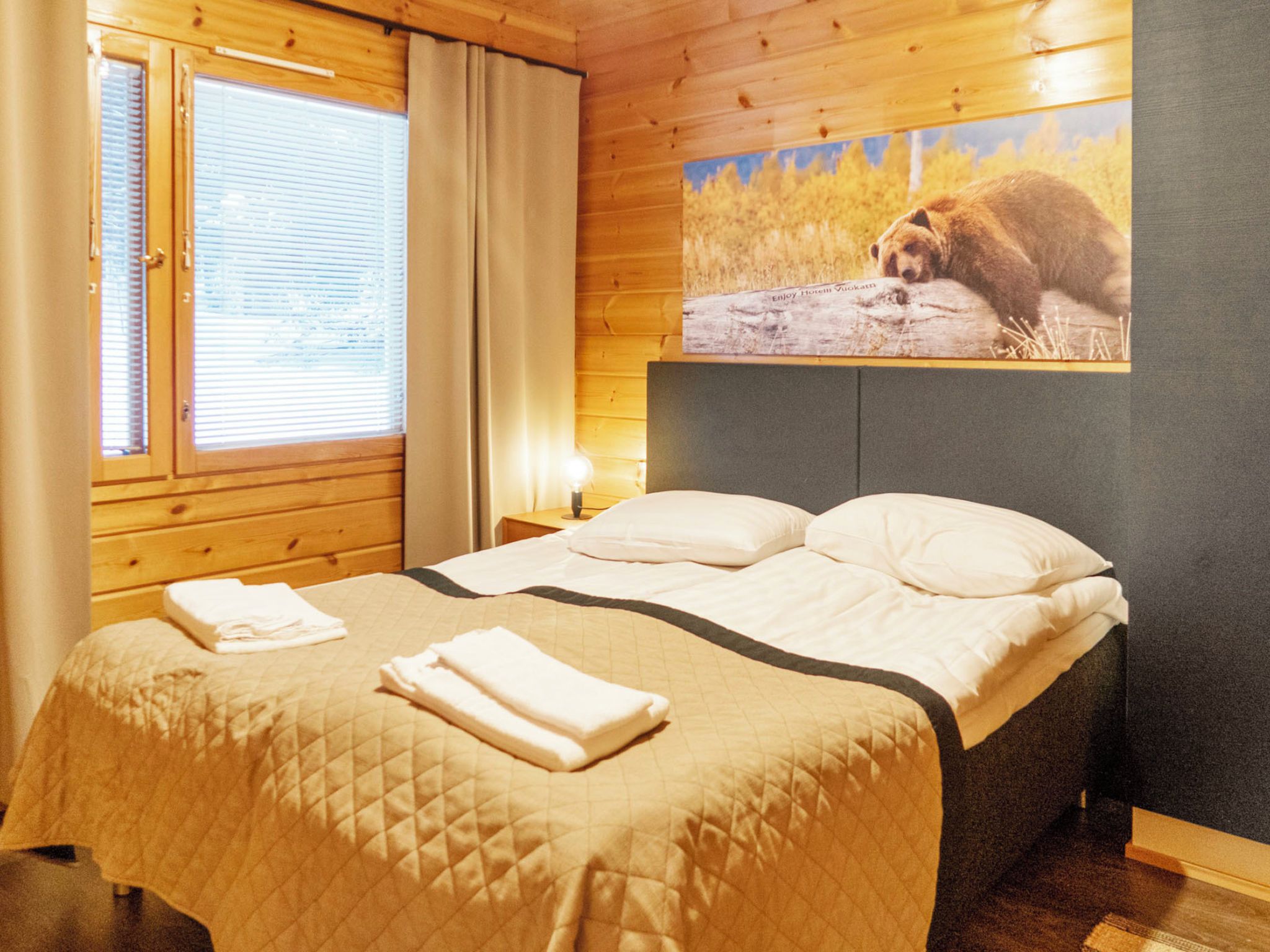 Una camera d'albergo con un letto, un comodino, una lampada e un quadro di un orso appeso al muro.