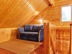 A cozy attic room with a wooden sloped ceiling, a blue sofa, and a woven rug. - Vuokatti villas ahma by Interhome (Sotkamo)