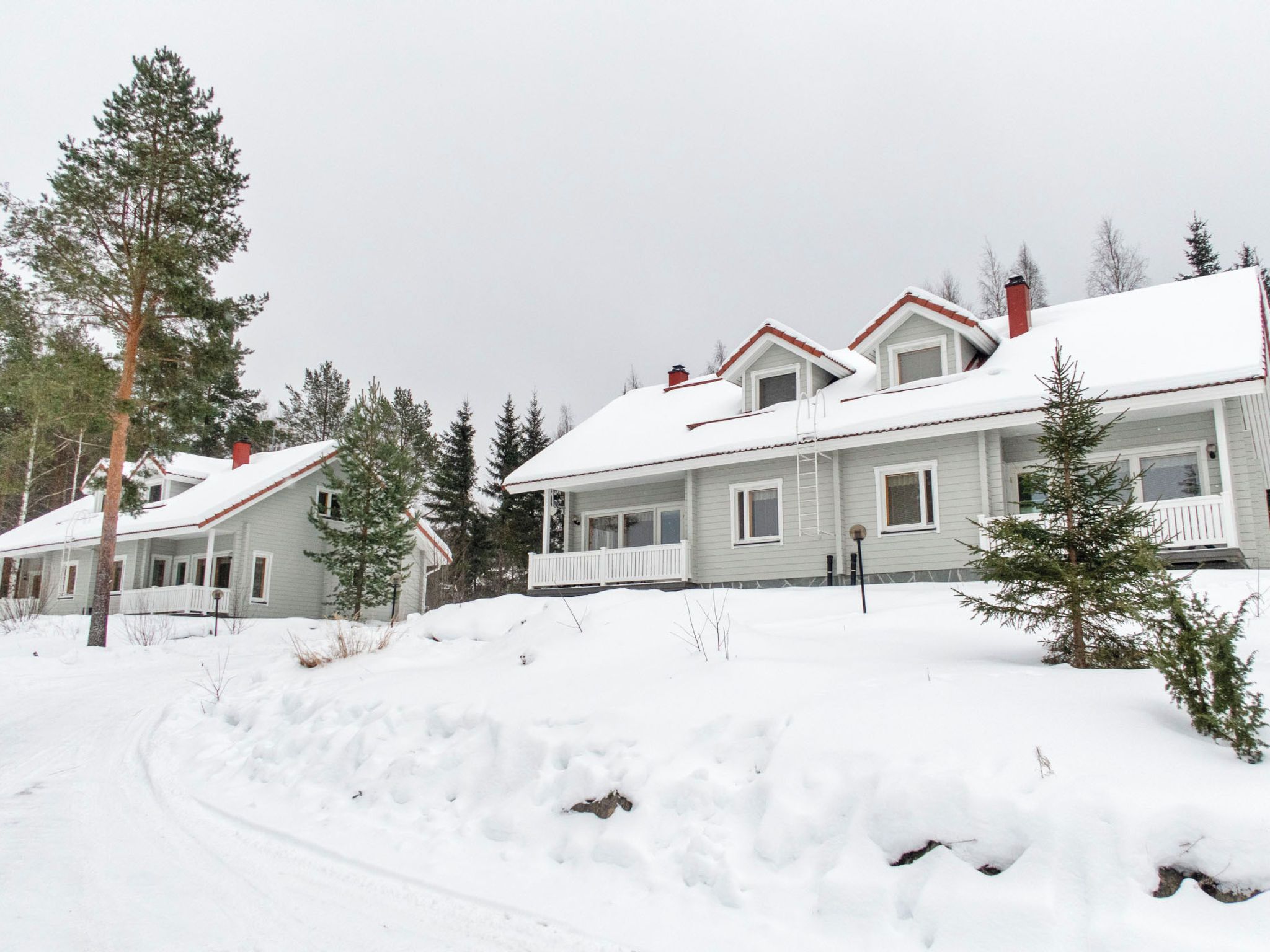 Une rangée de maisons à deux étages, dont les toits sont recouverts de neige et qui possèdent un petit porche.