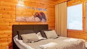 Une pièce aux murs lambrés, avec un lit, un tableau représentant un ours et une fenêtre équipée de stores.