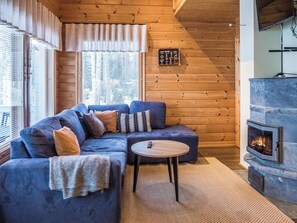 Ein gemütliches Blockhaus-Interieur mit einer Eckcouch, einem kleinen runden Tisch und einem Kamin aus Stein.