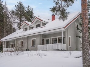 A two-story house with a covered porch and a red chimney, surrounded by snow-covered ground and trees. - Vuokatti villas susi by Interhome (Sotkamo)