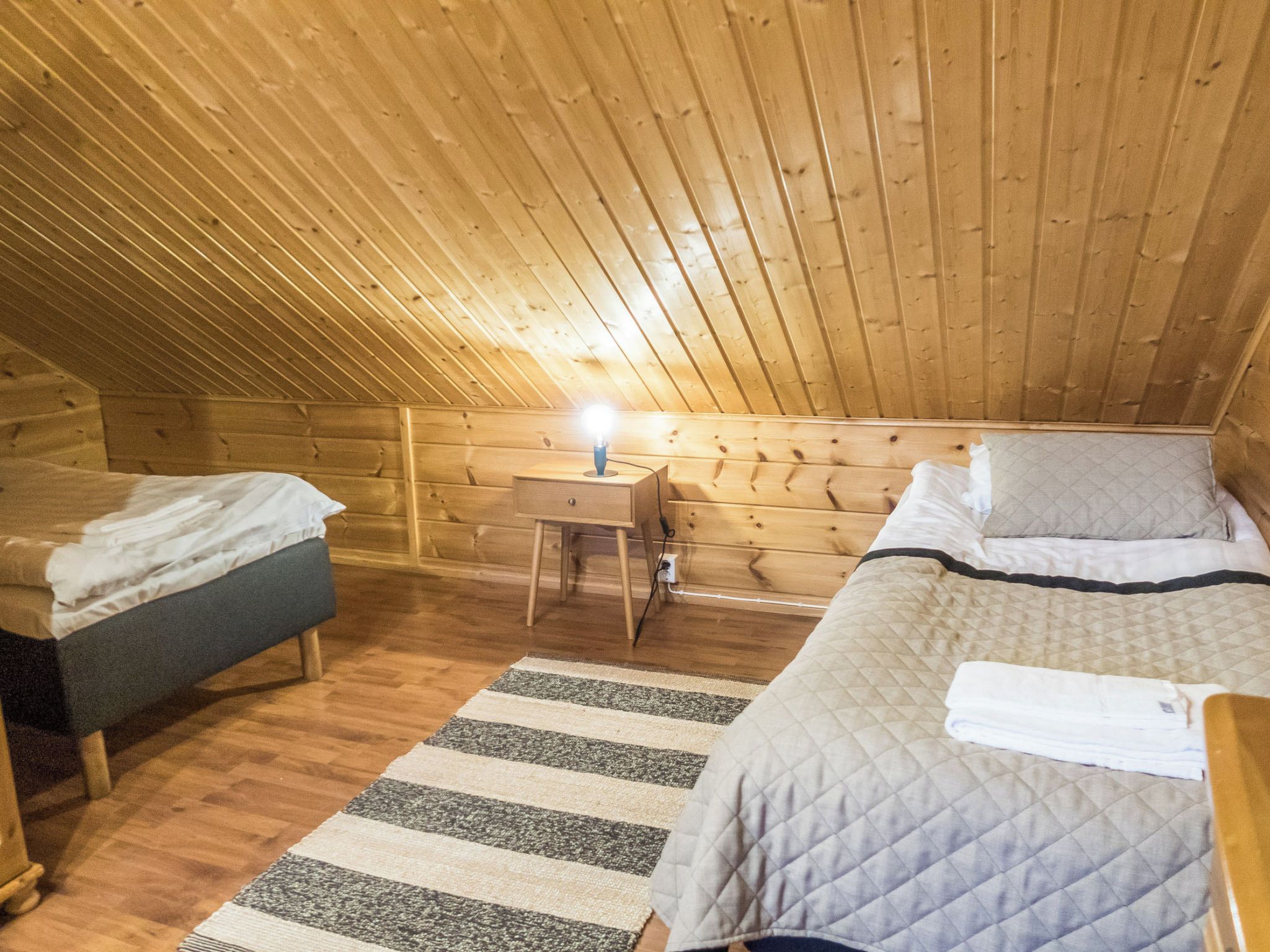 A cozy attic bedroom with two beds, a nightstand, and a lamp.