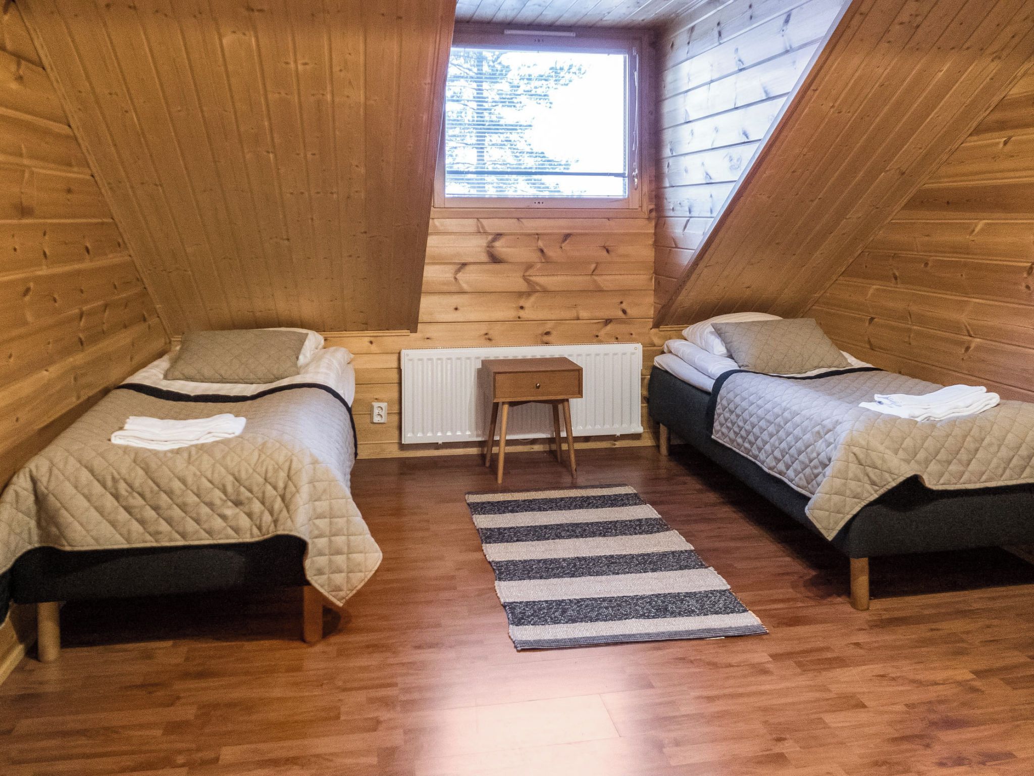 Une petite chambre mansardée avec deux lits, un radiateur et une fenêtre.