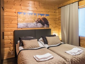 Ein Doppelbett mit gesteppter Bettdecke und zwei Kissen, ein hölzernes Kopfstück sowie ein an der Wand hängendes Bild von einem Bären.