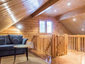 Une pièce mansardée chaleureuse avec un plafond en pente en bois, un canapé bleu, une petite table et une fenêtre avec des stores.