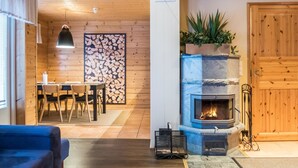A cozy living room with a fireplace, wooden walls, a dining area, and a blue sofa. - Vuokatti villas kettu by Interhome (Sotkamo)