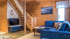 A wooden cabin interior with a staircase, a television, a sofa, and a painting on the wall. - Vuokatti villas kettu by Interhome (Sotkamo)