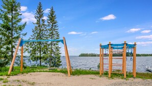 A playground with swings and climbing structures near a lake, surrounded by trees. - Vuokatti villas kettu by Interhome (Sotkamo)