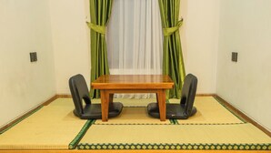 A room with a tatami mat floor, a wooden table, two black chairs, and green curtains. - Samurai Sanur Hotel (Denpasar)