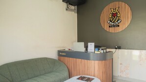A reception area with a wooden reception desk, a green sofa, and a marble table. - Samurai Sanur Hotel (Denpasar)