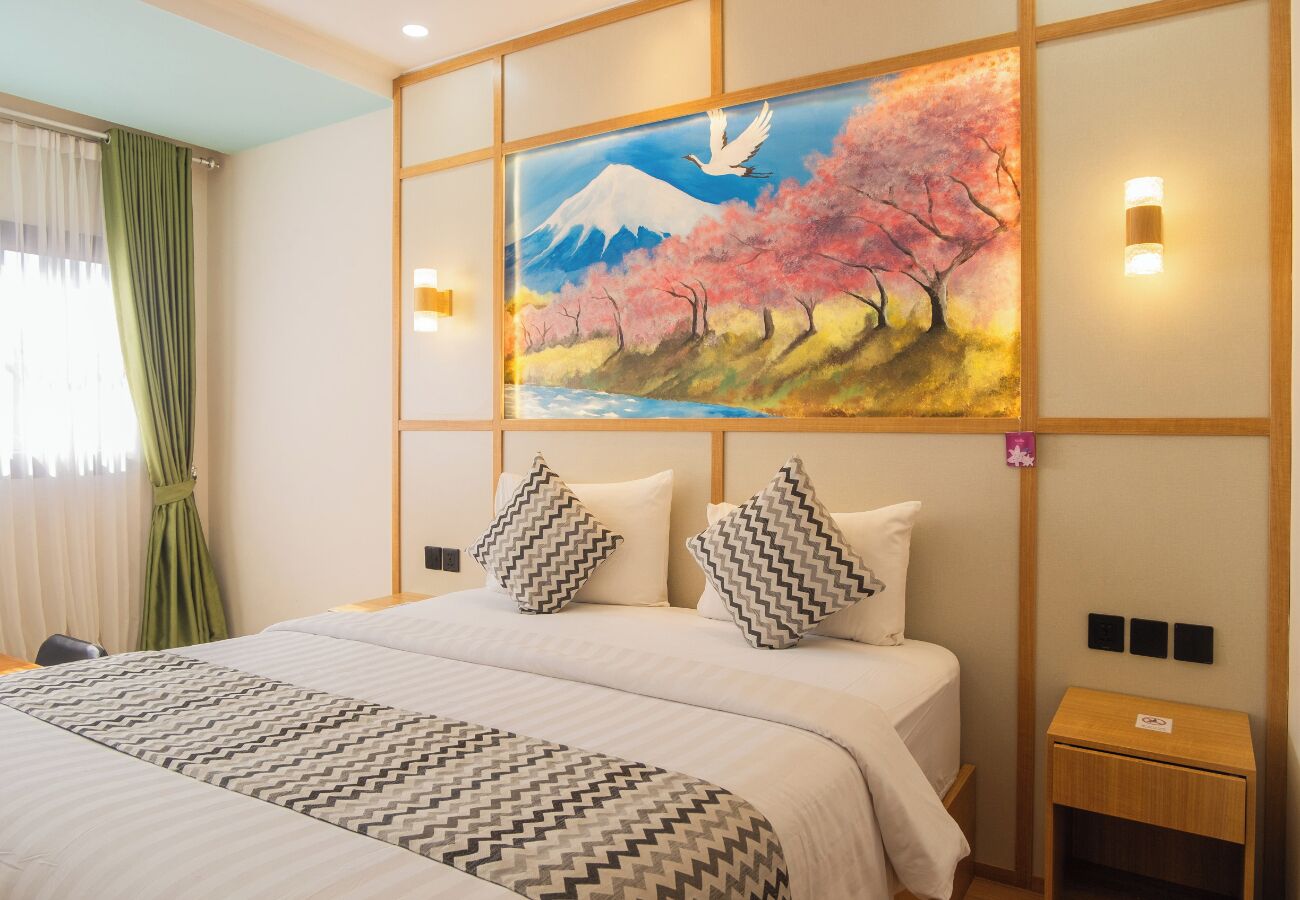 Ein Hotelzimmer mit einem großen Bett, einem Bild von Bergen und Kirschblüten sowie einem Nachttisch mit einer Lampe.