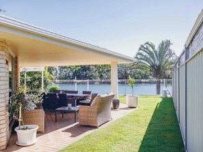 Une terrasse couverte avec des meubles d’extérieur, une petite pelouse et une vue sur un lac.