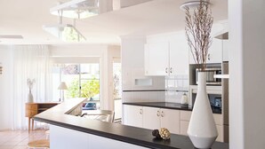 A modern kitchen with white cabinets, a black countertop, and a white vase with branches. - Waterfront - Kolora Lake House - Oceanstays (Yamba)