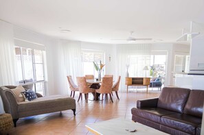 Un salon comprenant un canapé, un divan en cuir marron, une table à manger avec des chaises, et un coin cuisine à l’arrière-plan.