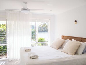 Une chambre d’hôtel avec un lit, des rideaux blancs, un ventilateur de plafond et une vue sur la verdure.