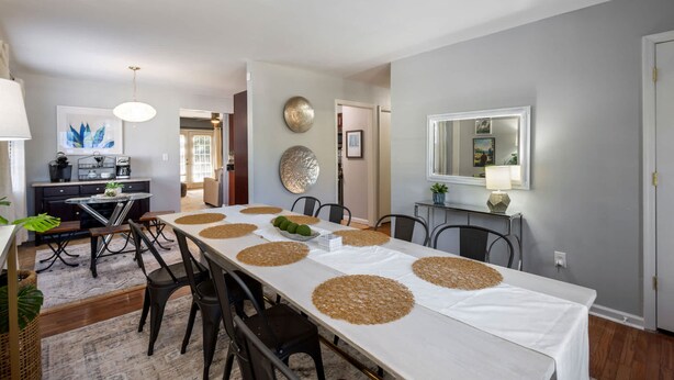 A dining area with a long table, chairs, and a kitchen in the background. - Hot Tub BBQ Retreat Spacious Backyard Pet-friendly (North Augusta)