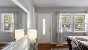 A room with a wooden floor, a white door with a stained glass window, a table with chairs, and a large mirror. - Hot Tub BBQ Retreat Spacious Backyard Pet-friendly (North Augusta)