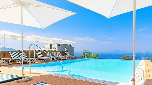 Zona de piscina con sillones de descanso y sombrillas, con vistas al mar azul y despejado.