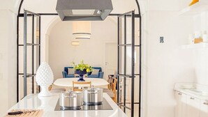 Una cocina moderna con una isla central, ollas de acero inoxidable y un florero azul con flores.