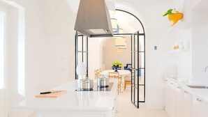 Una cocina moderna con armarios blancos, una isla central y un área de comedor visible a través de un arco.
