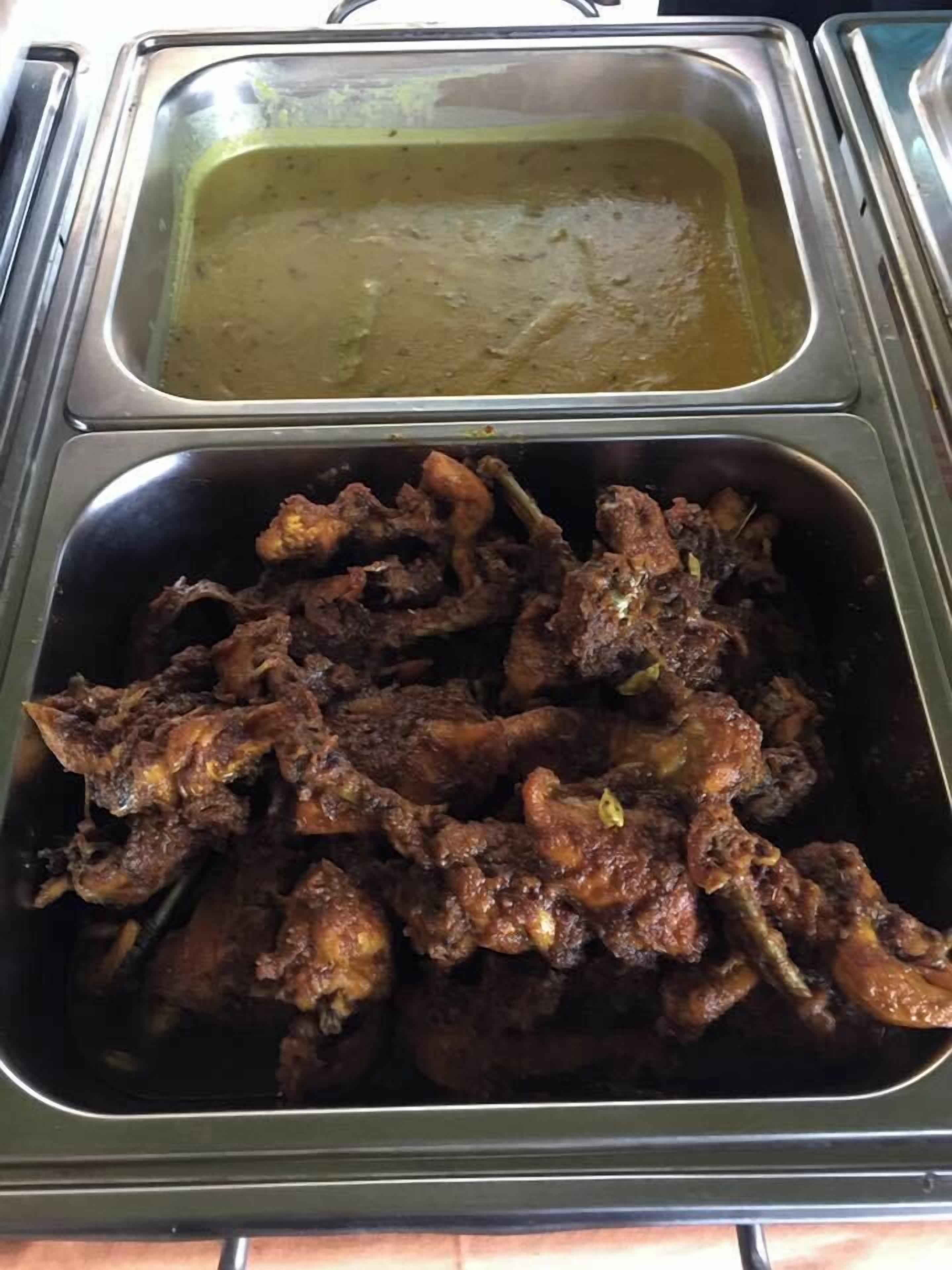 A buffet with two metal serving trays, one containing a green sauce and the other with a dark, seasoned meat dish.