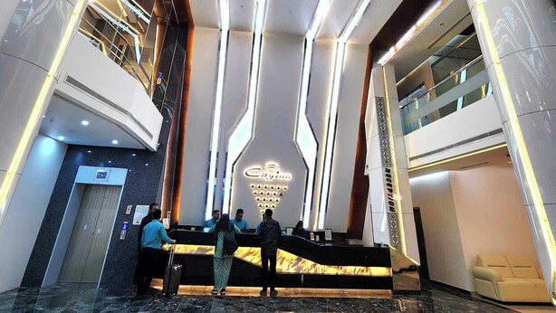 A modern hotel lobby with a central reception desk, a staircase, and a high ceiling with linear lighting. - City Inn Limited Khulna (Khulna)