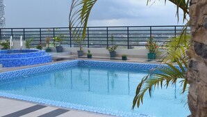 A rooftop swimming pool with a tiled edge, surrounded by potted plants and a stone wall. - City Inn Limited Khulna (Khulna)