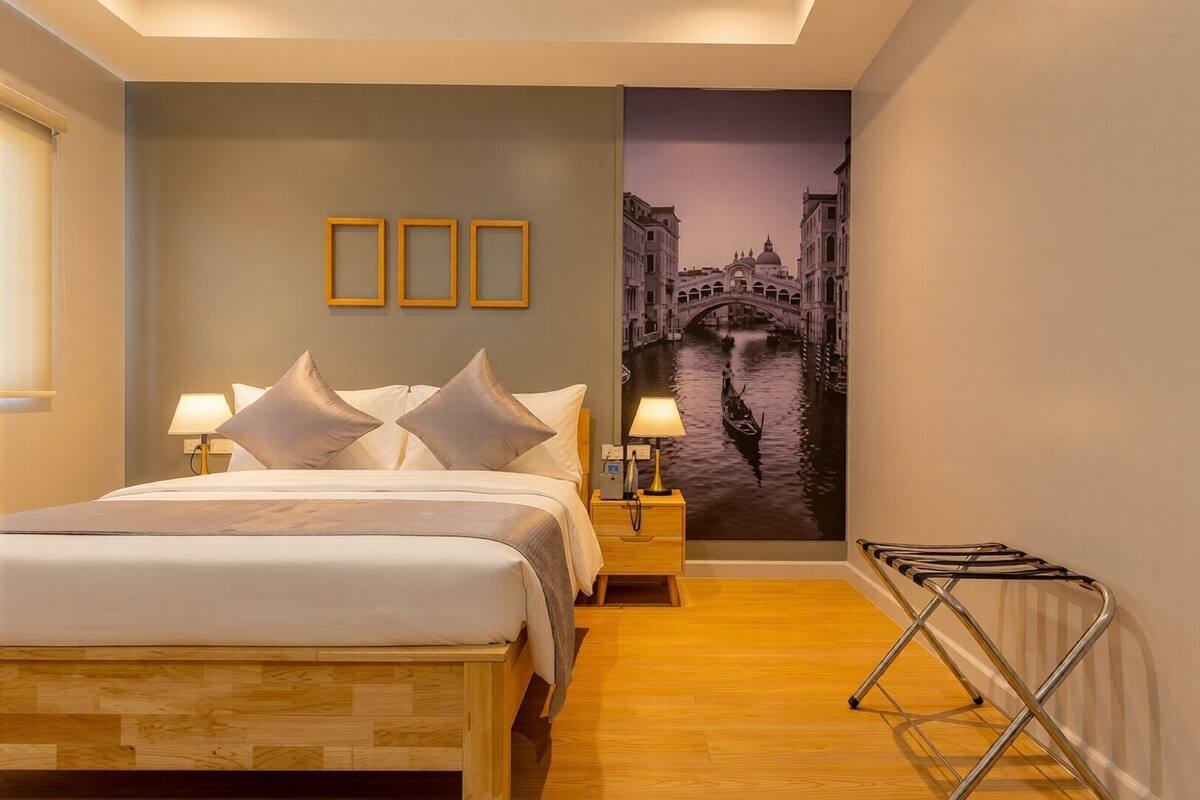 Une chambre d’hôtel avec un lit, deux tables de chevet avec des lampes, un plancher en bois, un mur orné d’une fresque représentant un paysage urbain et un radiateur.