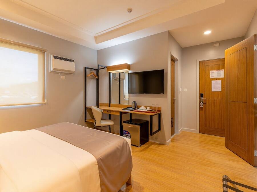 Habitación de hotel con cama, escritorio, silla, televisor y armario.