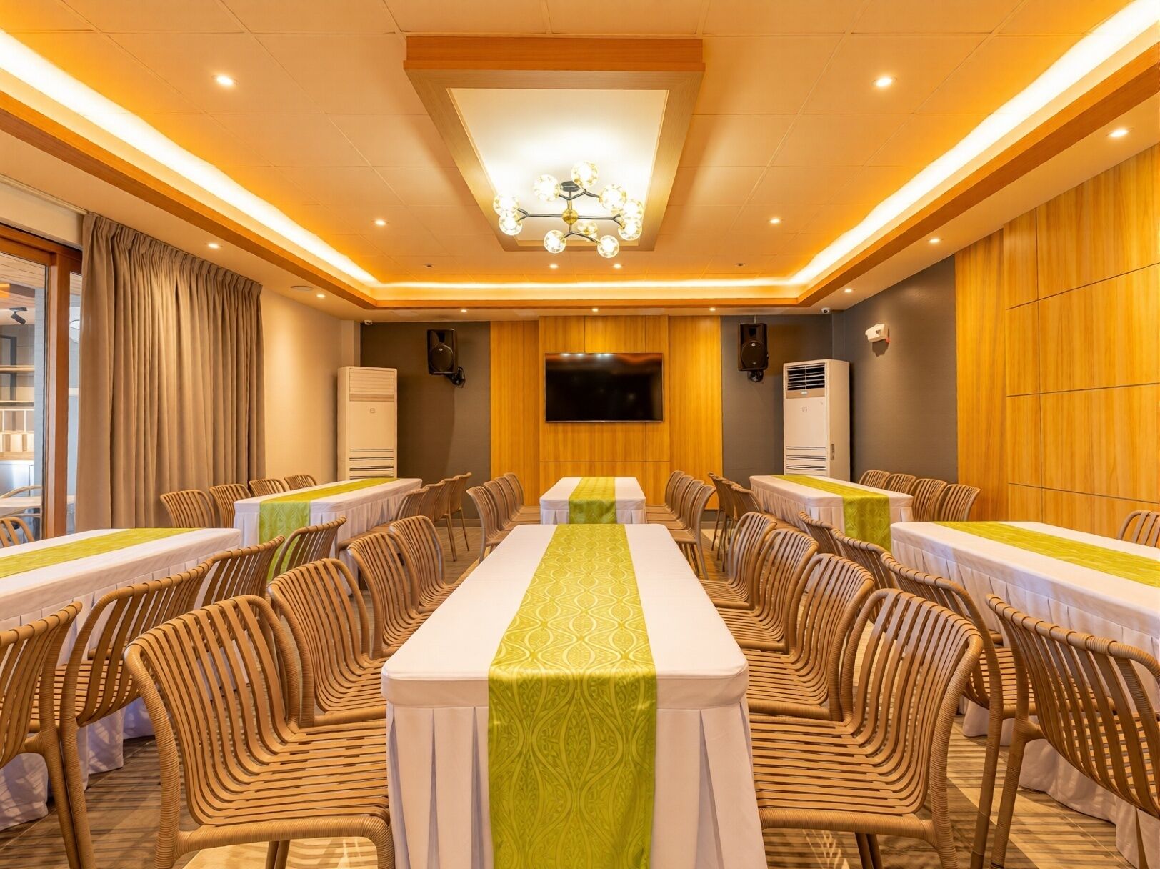 A conference room with tables, chairs, a chandelier, a TV, and speakers.