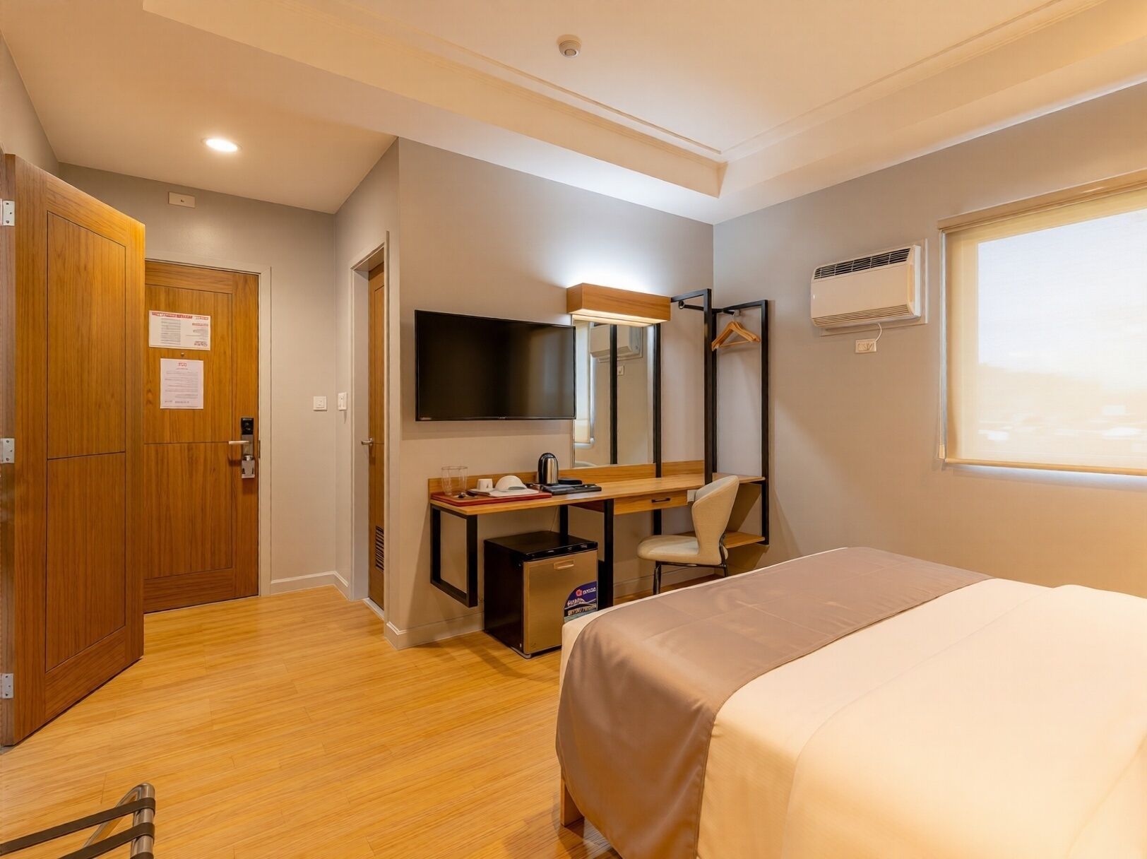 A hotel room with a bed, a desk with a chair, a TV, and a wardrobe.