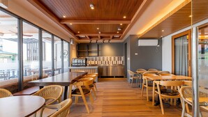 A modern interior with wooden floors, tables, and chairs, a kitchen area, and large windows. - Doña Manor Boutique Hotel (Olongapo)
