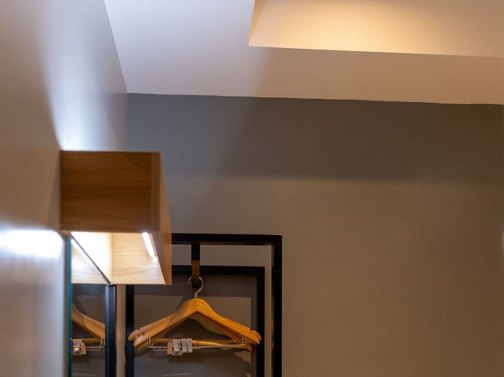 A room with a hanging wooden hanger, a mirror, and a ceiling light fixture.